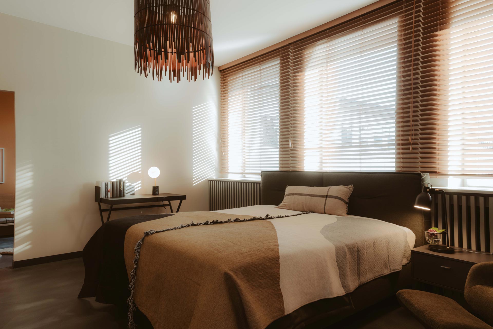 Modern eingerichtetes Schlafzimmer im FingerHome Showroom Frankenberg mit Doppelbett, Holzjalousien und stilvoller Beleuchtung.