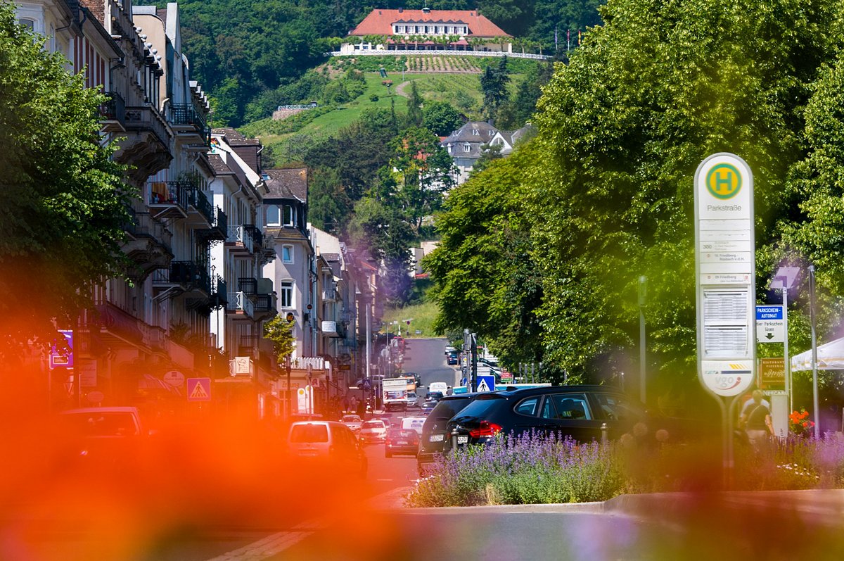 Straßenszene in Bad Nauheim mit historischen Stadthäusern, Bushaltestelle Parkstraße, blühenden Pflanzen im Vordergrund und Kurhaus auf dem Hügel.